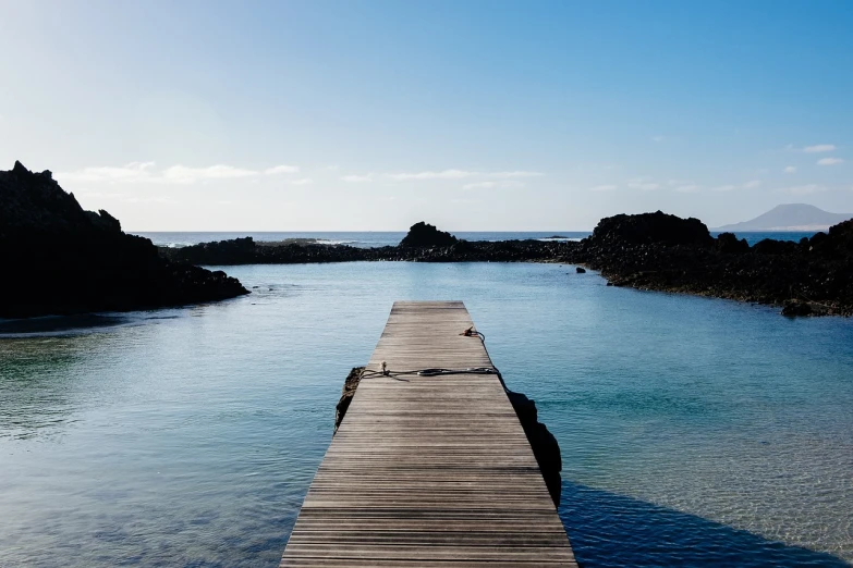 a dock in the middle of a body of water, a picture, by Simon Marmion, reunion island landscape, rock pools, mermaid in distance, unwind!