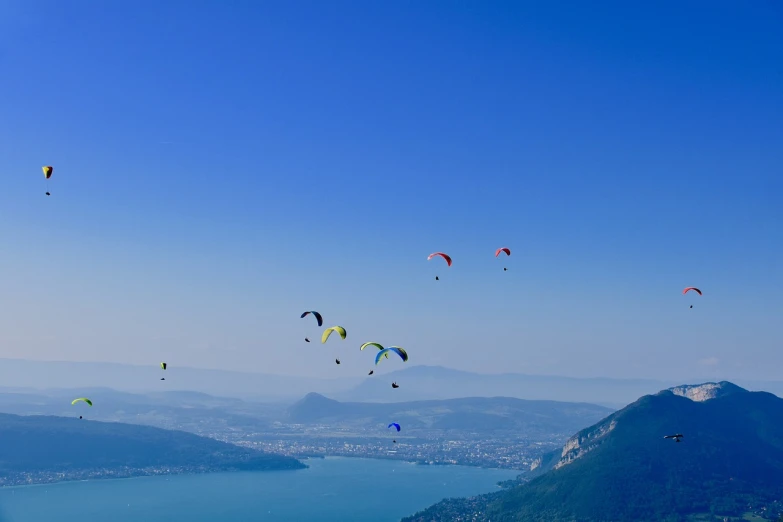 a group of people flying kites over a large body of water, by Cedric Peyravernay, shutterstock, 4k panoramic, mountaineous background, skydiving, view from the side”