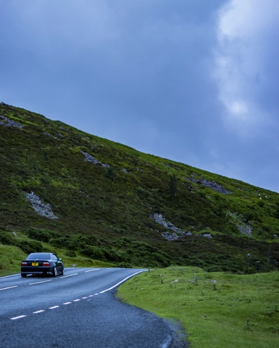 a car that is sitting on the side of a road, a picture, by Bedwyr Williams, unsplash, hillside, big overcast, 8 k photo, low angle photo