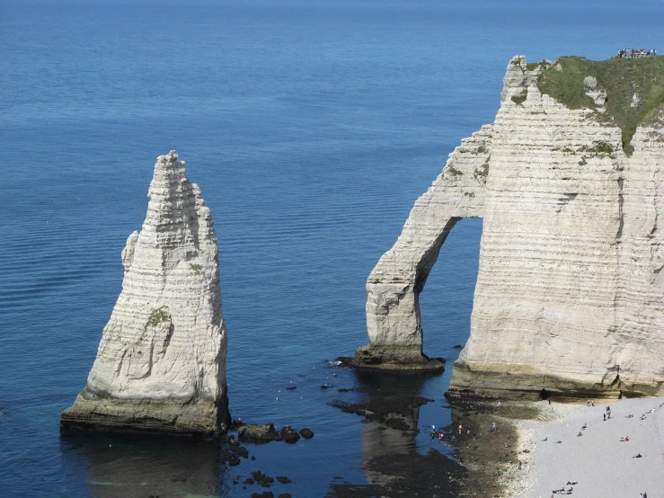 a couple of large rocks sticking out of the water, a picture, by Raphaël Collin, pexels, romanticism, massive arch, northern france, wikimedia commons, buttresses