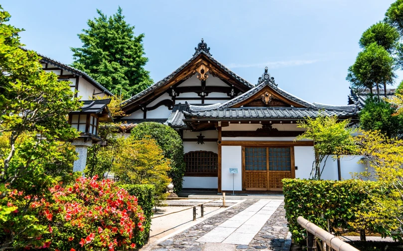 a white building surrounded by trees and bushes, a picture, inspired by Sesshū Tōyō, shutterstock, flared japanese black tile roof, old town, beautiful sunny day, wooden house