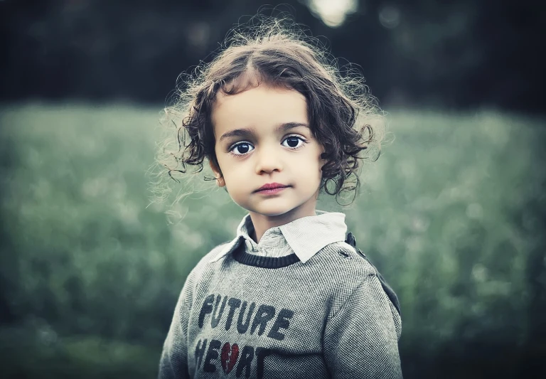 a little girl that is standing in the grass, a picture, by Lucia Peka, curly dark hair, serious sad look in his eyes, fine detail post processing, future activist