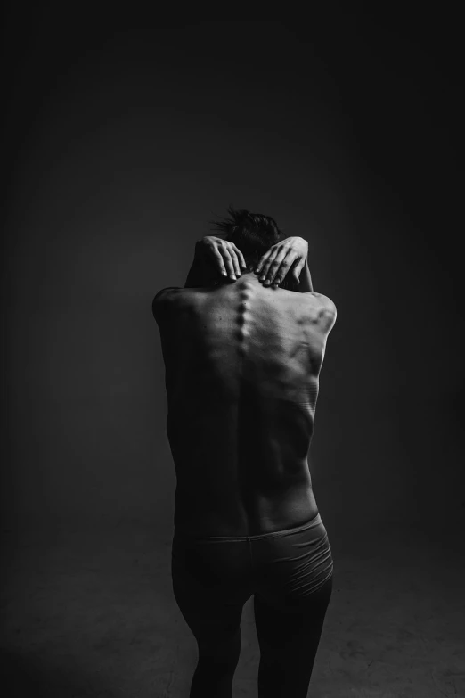 a black and white photo of a man with his back to the camera, by Matija Jama, unsplash contest winner, minimalism, in pain, woman posing, dark. studio lighting, with a spine crown