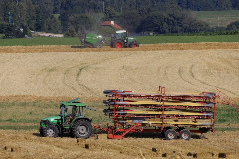 a tractor pulling a trailer filled with hay, by Hans Schwarz, flickr, green gas spreading across land, photograph credit: ap, with neat stubble, krzysztof kononowicz