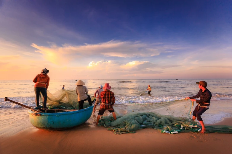 a group of people standing on top of a beach next to a boat, a picture, by Harold von Schmidt, shutterstock, netting, vietnam, on the beach at sunset, on a bright day