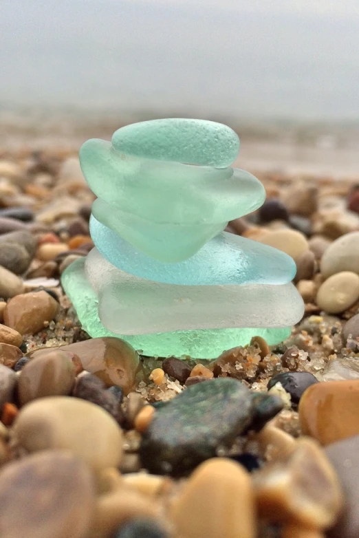 a stack of sea glass sitting on top of a pile of rocks, a macro photograph, inspired by Tom Wänerstrand, glass shader, cyan and green, 1505, soft shapes