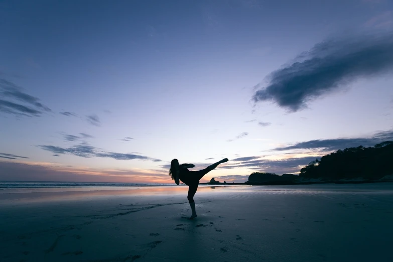 a woman doing a kick on the beach at sunset, new zealand, martial artist dryad, shot with a dslr, standing alone