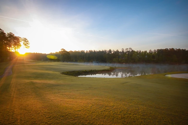 a golf course with a pond in the foreground, by Raymond Normand, shutterstock, fog golden hour, alabama, bottom angle, directional sunlight skewed shot