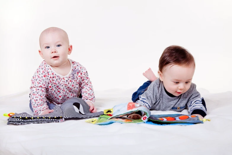 a couple of babies laying on top of a bed, a picture, by Juan O'Gorman, shutterstock, holding books, studio photo, from reading to playing games, studio portrait photo