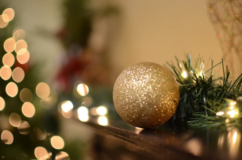 a gold christmas ornament sitting on top of a mantle, a picture, by Maksimilijan Vanka, pexels, backscatter orbs, 2 4 mm iso 8 0 0 color, soft light from the side, on a wooden desk