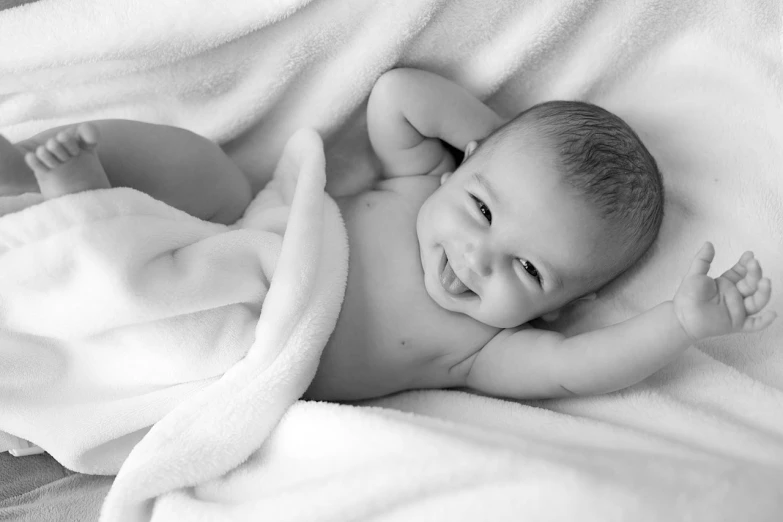 a black and white photo of a baby wrapped in a blanket, a black and white photo, pexels, relaxing and smiling at camera, smiling :: attractive, enhanced photo, laying down