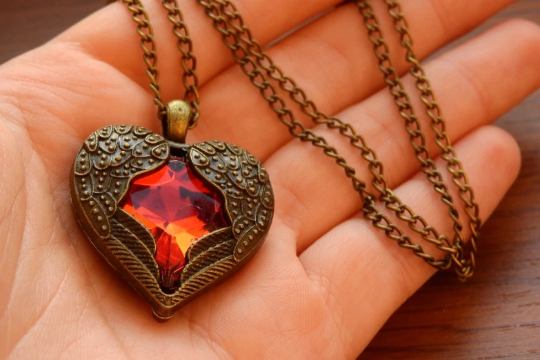 a close up of a person holding a heart shaped necklace, a picture, pixabay, art nouveau, fiery wings, rich colour and detail, faceted, close up shot of an amulet