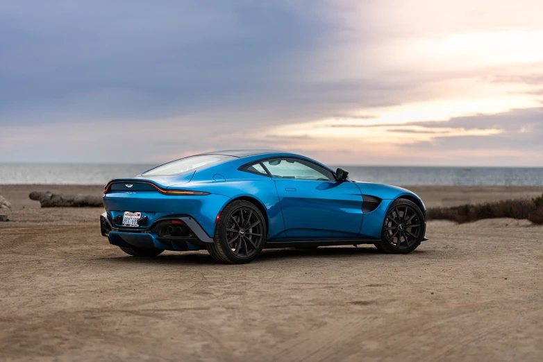 a blue sports car parked on a beach, a picture, by Austin English, unsplash, renaissance, aston martin, right side profile, back arched, glossy surface