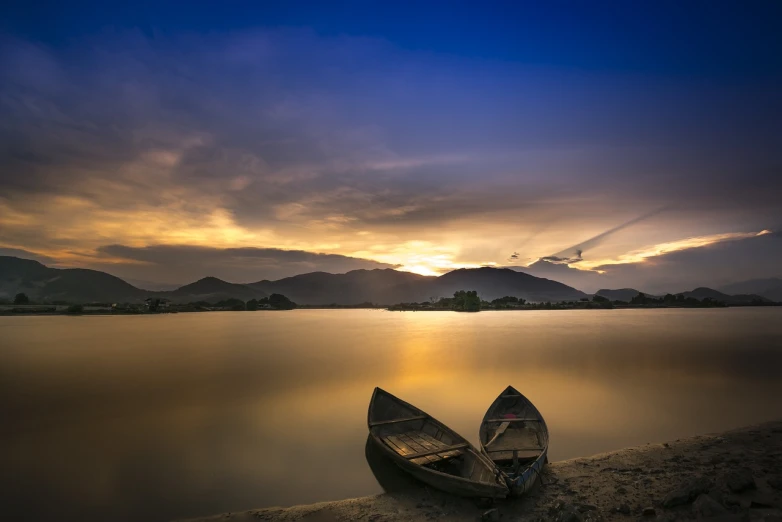 a couple of boats sitting on top of a lake, a picture, by Shen Quan, shutterstock, long exposure photo, lonely scenery yet peaceful!!, sunset photo, very beautiful photo