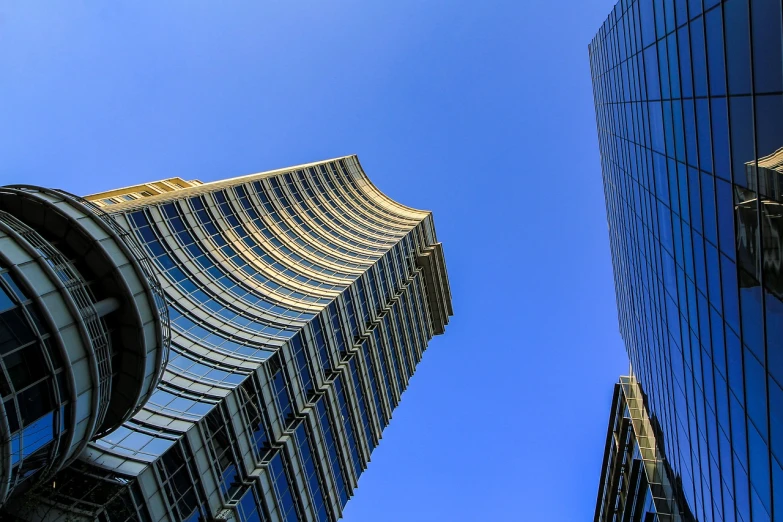 a couple of tall buildings next to each other, a stock photo, inspired by Zaha Hadid, flickr, golden curve structure, blue sky above, cinematic view from lower angle, 2 4 mm iso 8 0 0 color