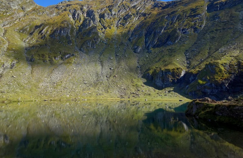 a body of water with a mountain in the background, by Werner Andermatt, flickr, hurufiyya, vertical portrait, reflections. shady, steep cliffs, mini lake