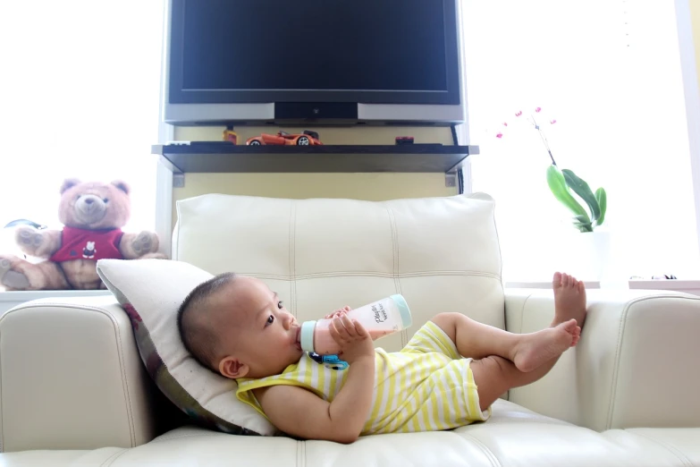 a baby laying on a couch drinking from a bottle, a picture, happening, tv, istockphoto, jinyiwei, milky white skin