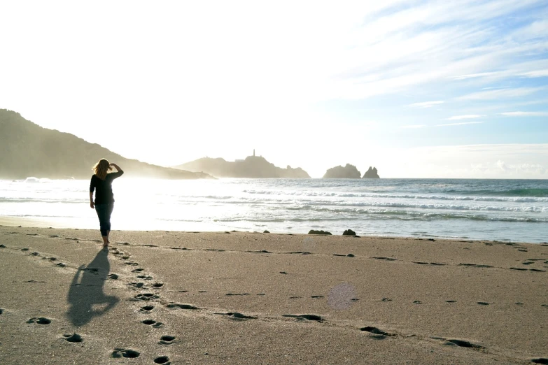 a person walking on a beach next to the ocean, a photo, cornwall, backlight photo sample, minas tirith in the background, pointing to heaven