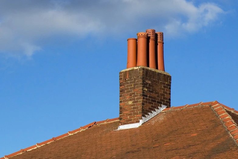 a clock mounted to the side of a brick building, by Lee Loughridge, roofing tiles texture, chimney with smoke, blue sky, tubes