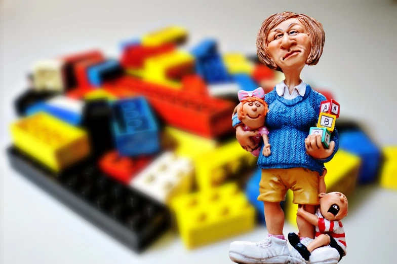 a figurine of a woman holding a baby next to a pile of toys, inspired by Sam Havadtoy, trending on pixabay, toyism, bricks, 3d render senior artist, portrait of angela merkel, highly detailed composition