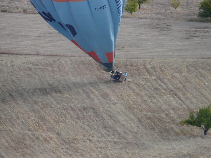 a blue and orange hot air balloon flying over a field, a photo, figuration libre, car shot, stuck in the ground, very high angle view, watch photo