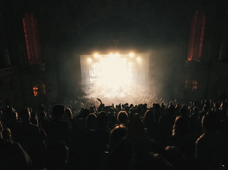 a crowd of people standing in front of a stage, a picture, by Karl Buesgen, pexels contest winner, faded and dusty, epic lighting from above, big windows, instrument