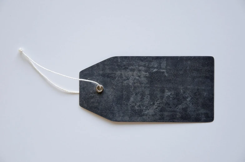 a black tag sitting on top of a white table, unsplash, sōsaku hanga, fine texture structure, 2 1 0 mm, chalkboard, upcycled