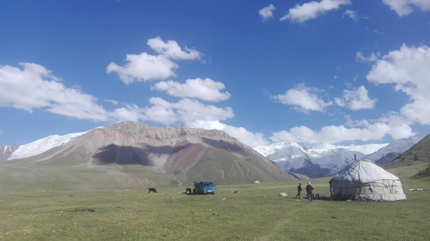 a group of people standing on top of a lush green field, by Muggur, truck, high mountains, ash thorp khyzyl saleem, grazing