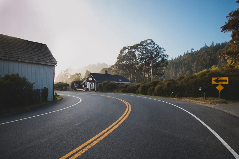 a curve in the road with a house in the background, by Andrew Domachowski, pexels, bay area, simple nostalgic, highway 5 0, round about to start