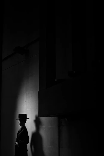 a black and white photo of a man in a hat, by Andrew Domachowski, minimalism, lights and shadows, captured on canon eos r 6, silhouette :7, architecture mystery