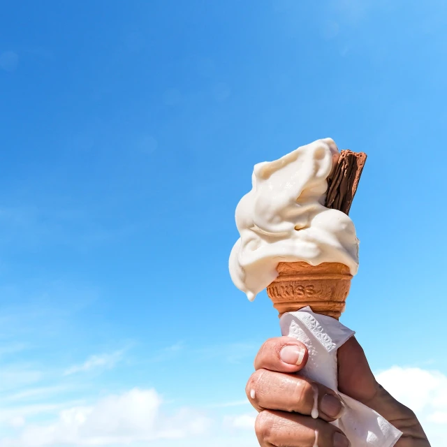 a person holding an ice cream cone in their hand, a picture, by Etienne Delessert, shutterstock, blue skies, closeup at the food, stock footage