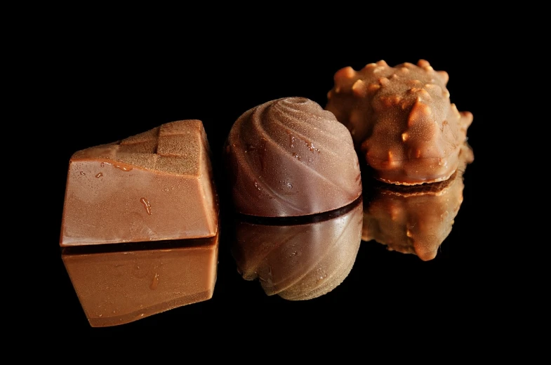 a group of chocolates sitting on top of a table, a picture, by Aleksander Gierymski, in front of a black background, reflection, three fourths view, medium head to shoulder shot