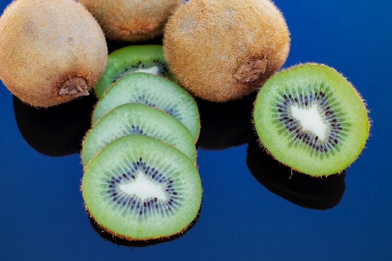 a group of kiwis sitting on top of a blue surface, green and black colors, istockphoto, plates of fruit, mirrored