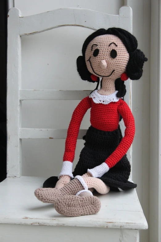 a crocheted doll sitting on a chair, inspired by Louise Abbéma, with black hair, with a red skirt, comic character, sitting on the floor
