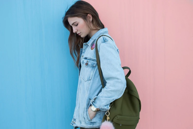 a woman leaning against a pink and blue wall, shutterstock, green colored bomber jacket, school bag, wearing double denim, backlit shot girl in parka