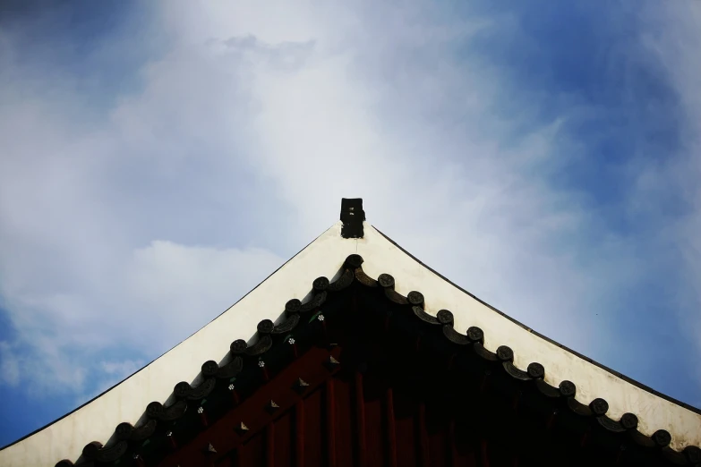 a bird is perched on the roof of a building, inspired by Sesshū Tōyō, minimalism, korean traditional palace, focus on the sky, ceremonial clouds, bottom angle