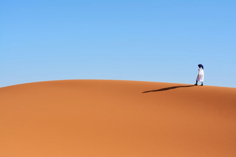 a person standing on top of a sand dune, inspired by Scarlett Hooft Graafland, unsplash, minimalism, marrakech, strong blue and orange colors, lone person in the distance, high detail photo of a deserted