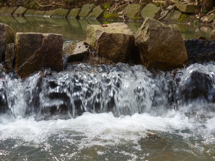 a close up of a waterfall with rocks in the background, a picture, nature photo, water flowing through the sewer, datastream or river, illinois