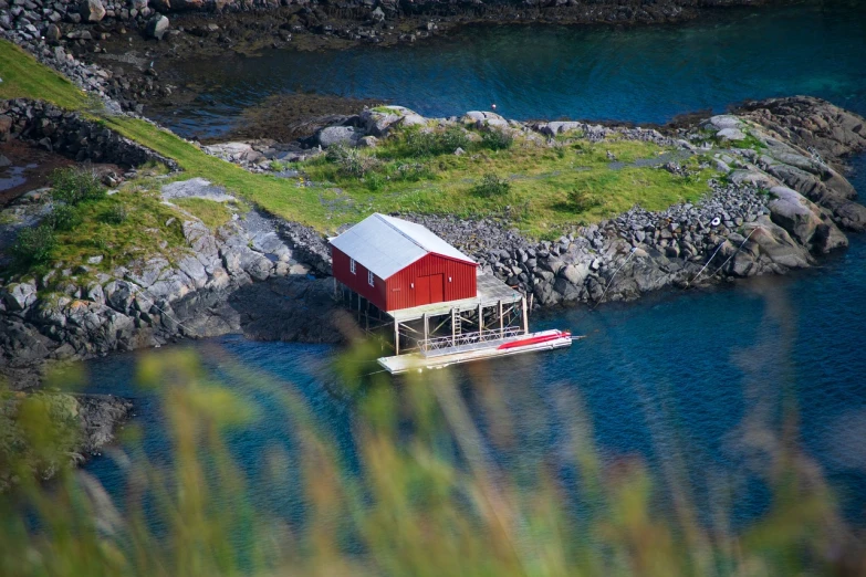 a red boat sitting on top of a body of water, a tilt shift photo, by John Murdoch, flickr, plein air, hut, norway, modern setting, built around ocean
