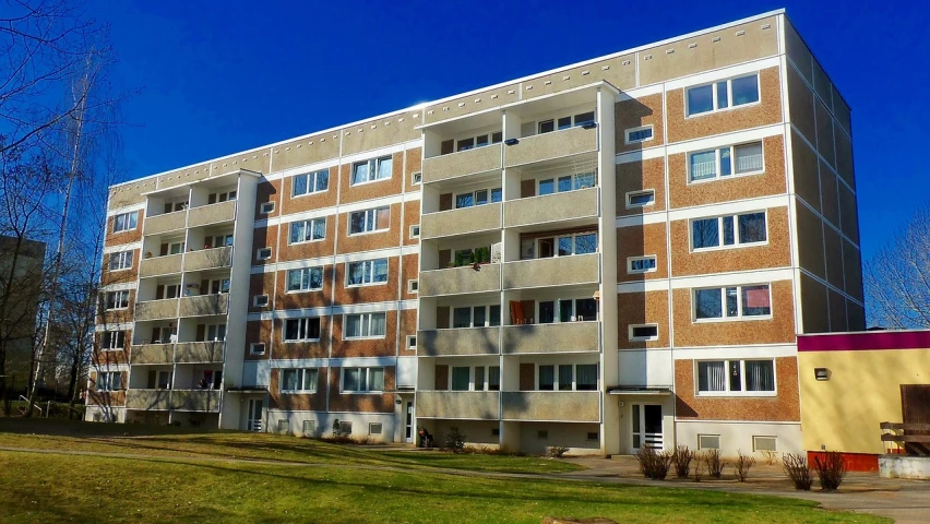 a tall brick building sitting on top of a lush green field, by Jaakko Mattila, pixabay, bauhaus, soviet apartment buildings, anato finnstark. front view, panels, crenellated balconies