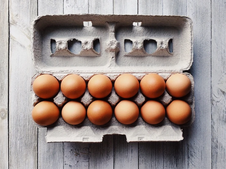 a carton of eggs sitting on top of a wooden table, a picture, unsplash, instagram photo, foodphoto, grain”