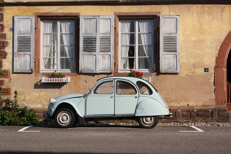 a small blue car parked in front of a building, by Etienne Delessert, large windows to french town, stained antique copper car paint, cute future vehicles, white and pale blue