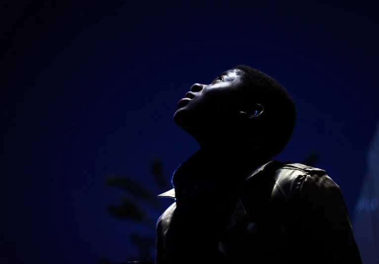 a man standing in the dark with a cell phone in his hand, a portrait, hurufiyya, looking up into the sky, emmanuel shiru, in profile, face is brightly lit