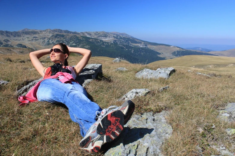 a woman sitting on top of a grass covered hillside, with sunglass, lying pose on stones, transylvania, camera photo