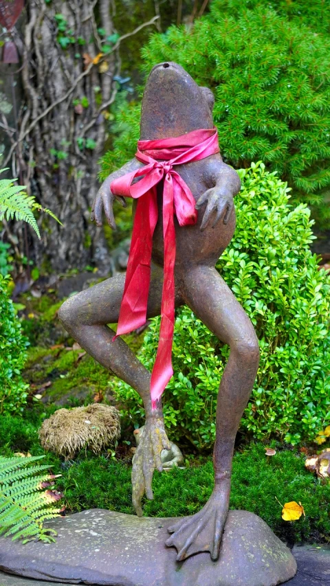 a statue of a frog with a red scarf around its neck, a statue, inspired by Aristide Maillol, chinese ribbon dance, satyr, obi strip, lush surroundings