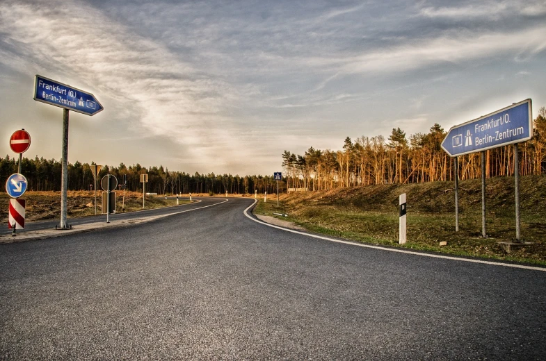 a couple of street signs sitting on the side of a road, a picture, by Thomas Häfner, flickr, realism, sunset panorama, german forest, curved, smooth curves