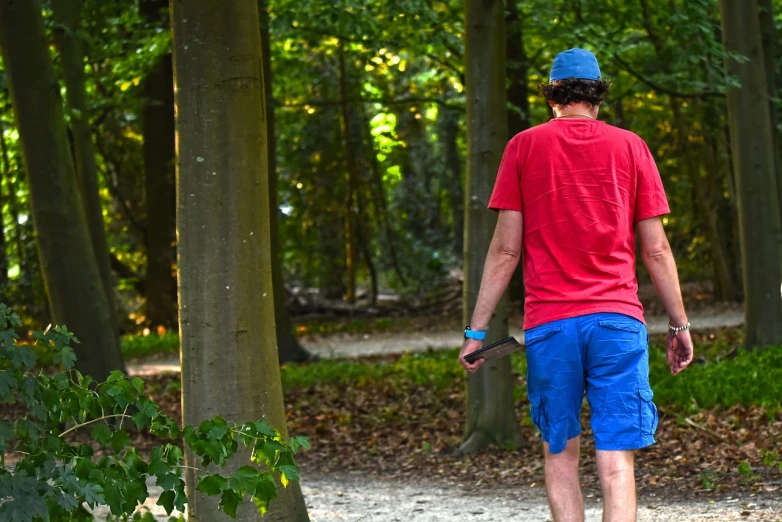 a man riding a skateboard down a dirt road, a picture, by Jan Tengnagel, process art, red shirt brown pants, walking around in a forest, red and blue back light, wearing shorts and t shirt