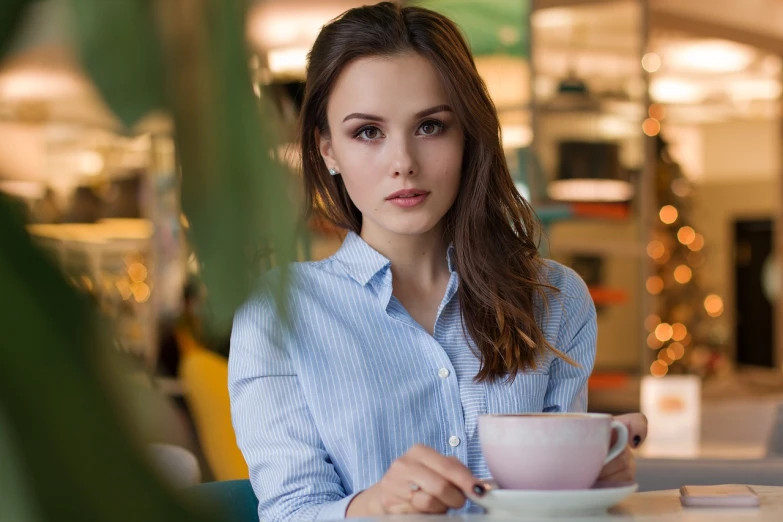 a woman sitting at a table with a cup of coffee, a portrait, shutterstock, beautiful alluring teen, natali portman, avatar image, unedited