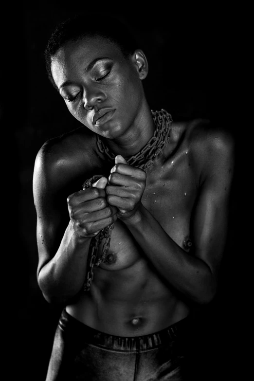a black and white photo of a man with a chain around his neck, a portrait, inspired by Chinwe Chukwuogo-Roy, art photography, hands behind her body pose!, high contrast studio lighting, chains broken on hands, impassioned