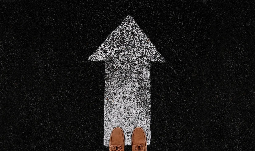 a pair of brown shoes standing in front of a white arrow, a photo, trending on pexels, standing with a black background, wet asphalt, standing in outer space, top down perspective